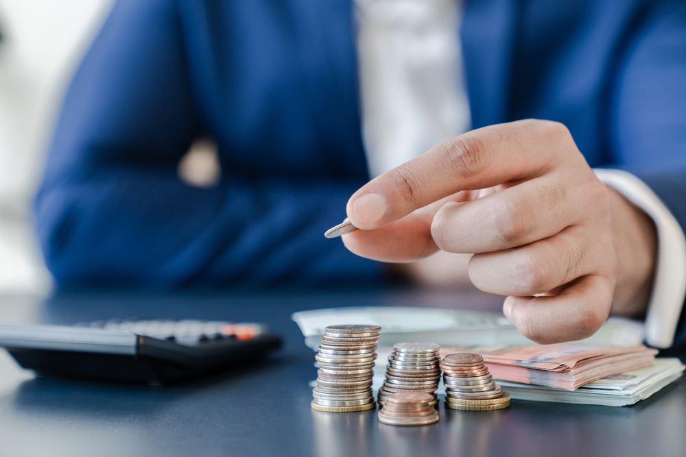 Hand legt Münzen auf einen Stapel neben einem Taschenrechner